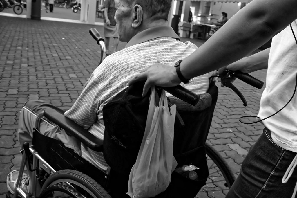 Homme en fauteuil roulant aidé par un proche