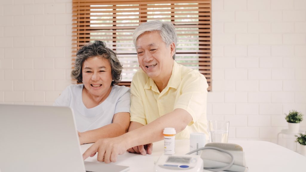 Pareja de ancianos asiáticos usando una computadora portátil conferencia con el médico sobre la información de la medicina en la sala de estar, pareja usando el tiempo juntos mientras están acostados en el sofá de la casa. Concepto de salud familiar en el hogar.