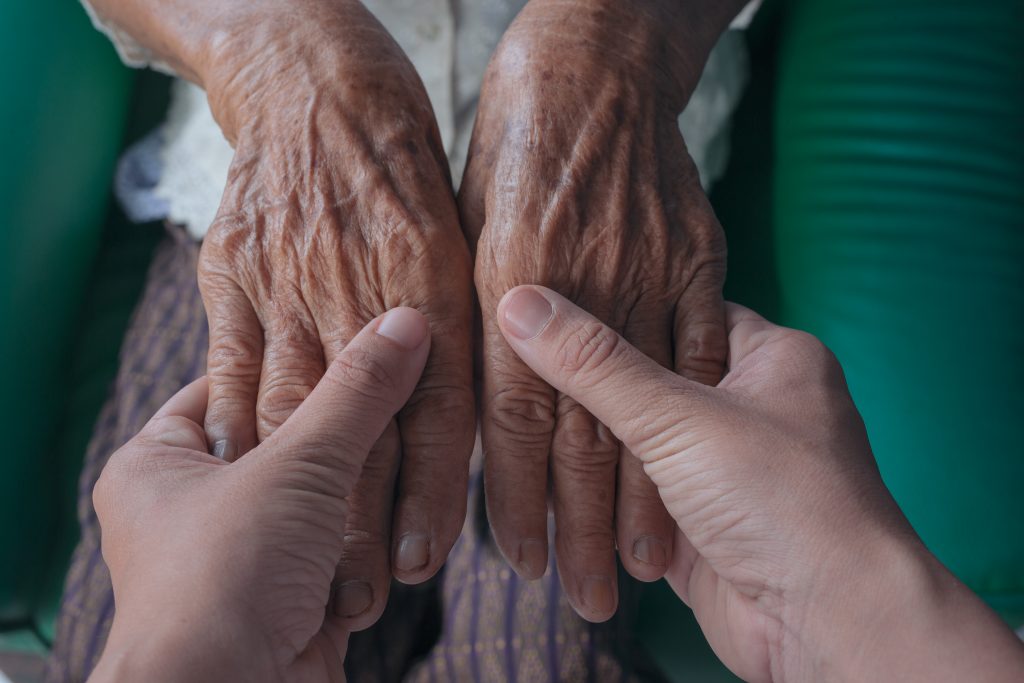 Una mujer joven sosteniendo la mano de una anciana para ayudarla.
