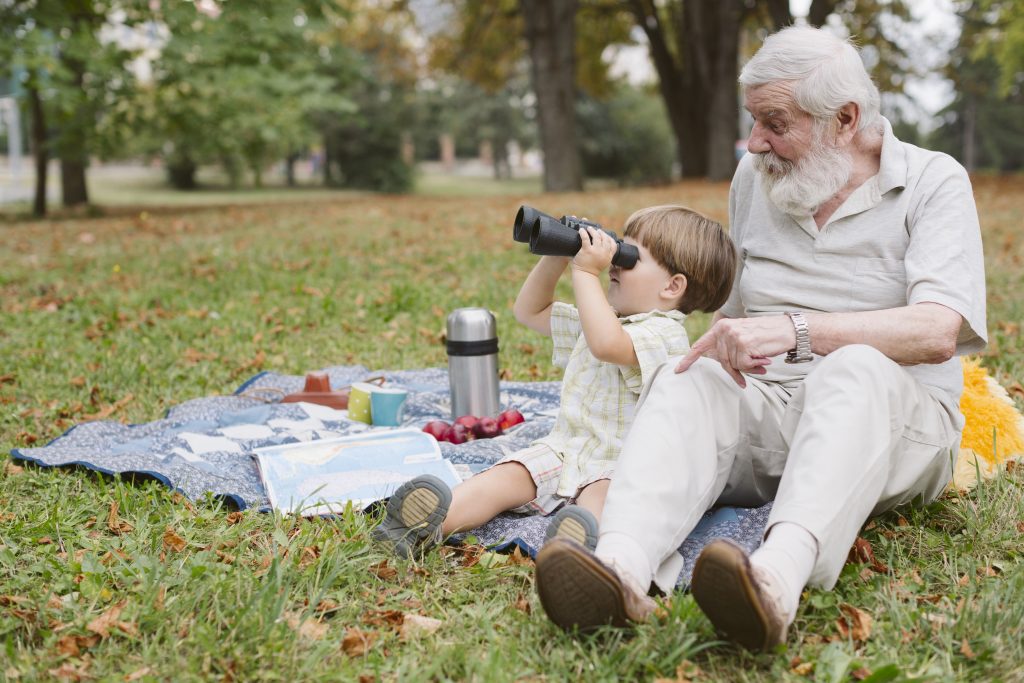 Abuelo con su nieto sentados sobre pastos mirando de un lado. 